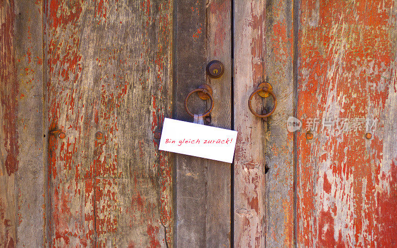 “Bin Gleich Zurüch”在旧风化的红色门上的注释